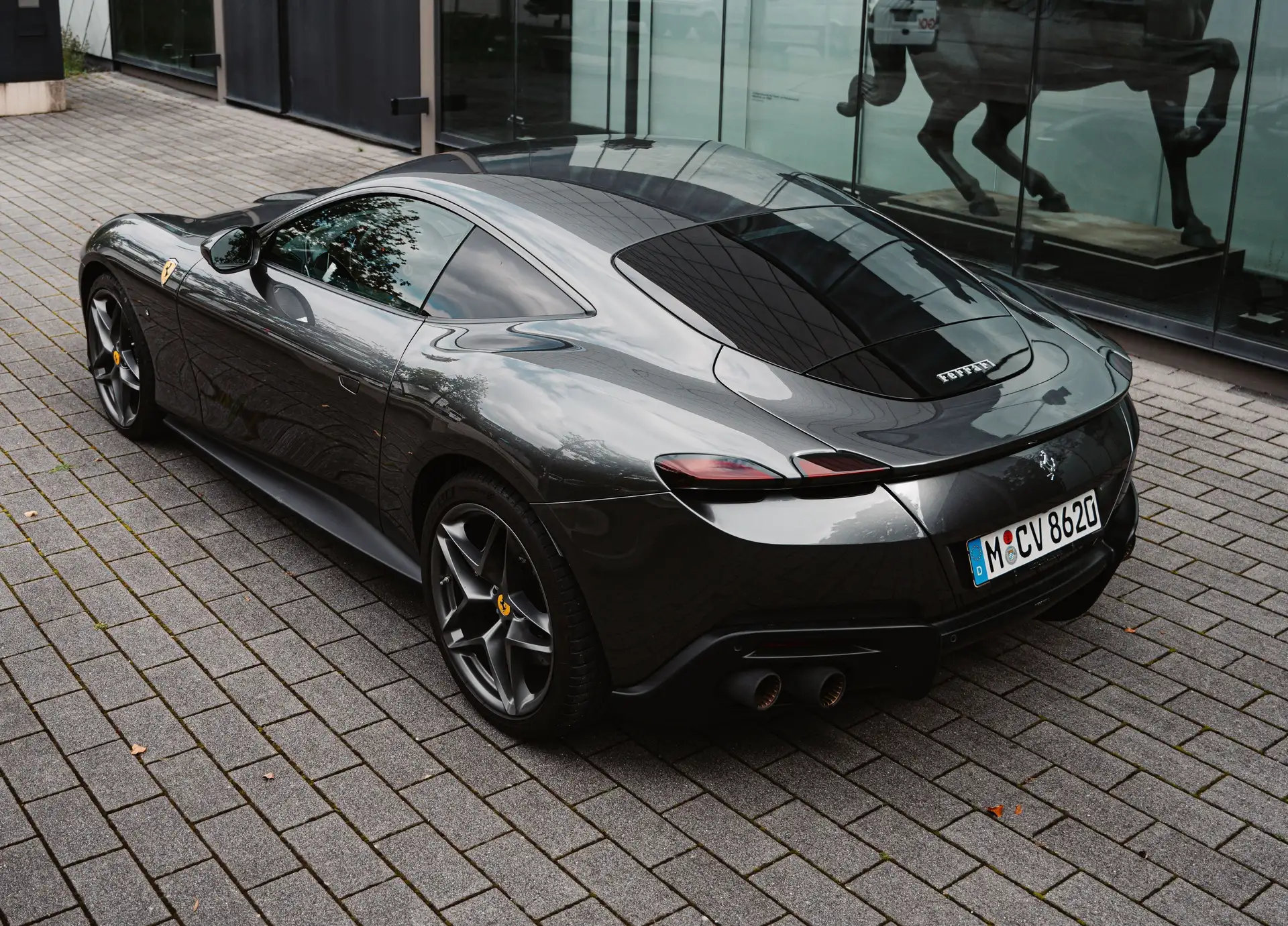 A gray Ferrari Roma in the rear view in front of a Pegasus.